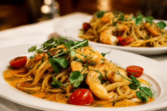 Two plates of shrimp linguine topped with fresh microgreens and halved cherry tomatoes in a light sauce.