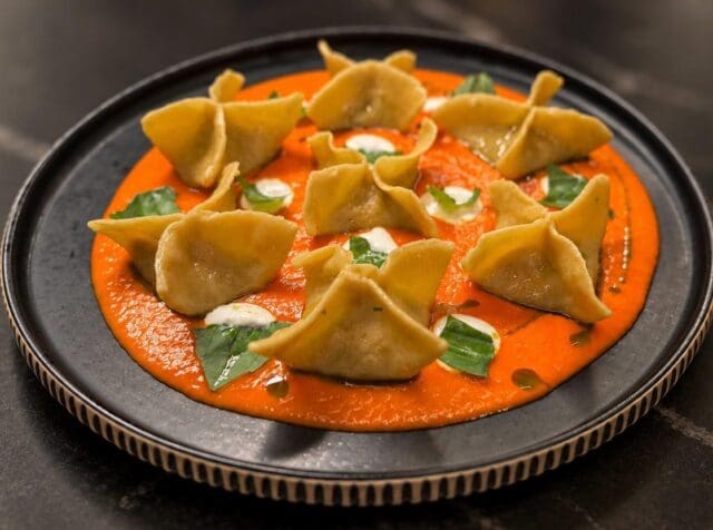 Stuffed pasta dumplings served in a pool of orange sauce garnished with basil and dollops of white cream.